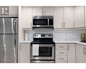 A modern kitchen with a stainless steel refrigerator, a microwave above the stove, and white cabinets.