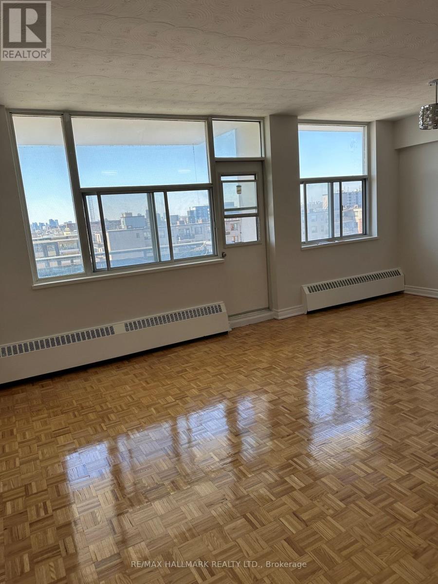 A large empty room with wooden floors and windows overlooking a city.