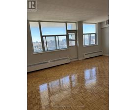 A large empty room with wooden floors and windows overlooking a city.