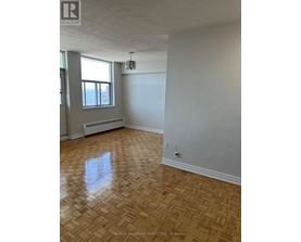 A room with a wooden floor and a window with a radiator beneath it.