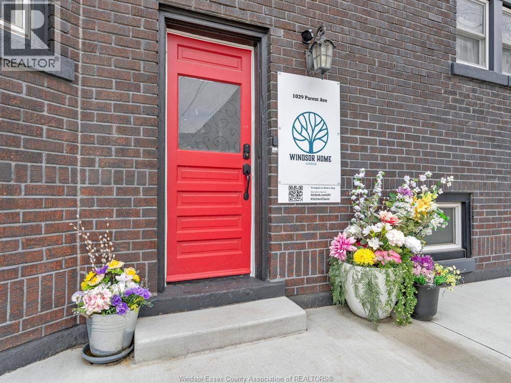 A red door with a sign that says "1003 Pine Ave Windsor Home" in front of a brick building.