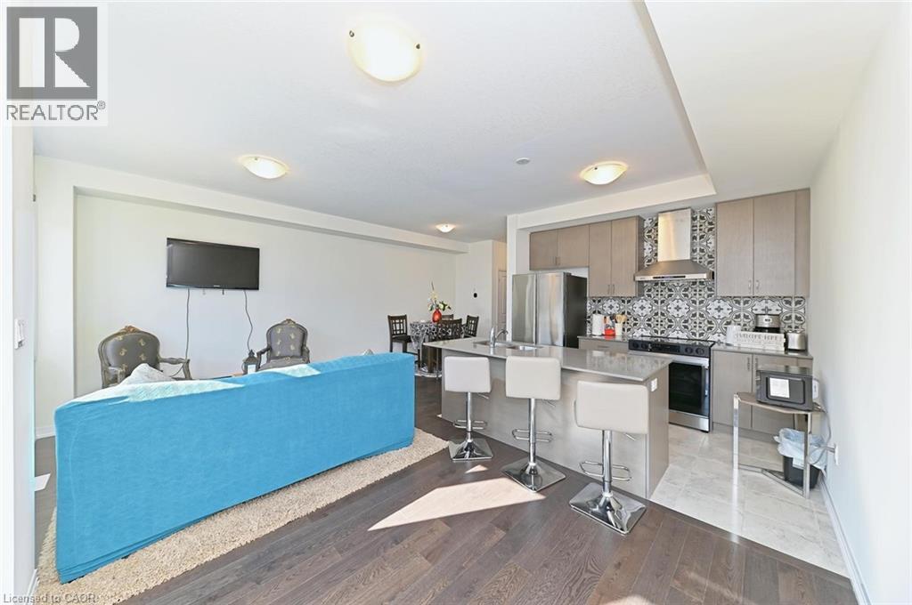 A blue couch is in the middle of a living room with a television and a kitchen area in the background.