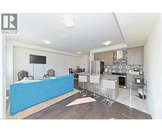 A blue couch is in the middle of a living room with a television and a kitchen area in the background.