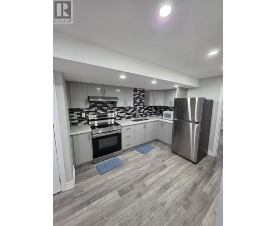 A modern kitchen with a stainless steel refrigerator and wooden flooring.