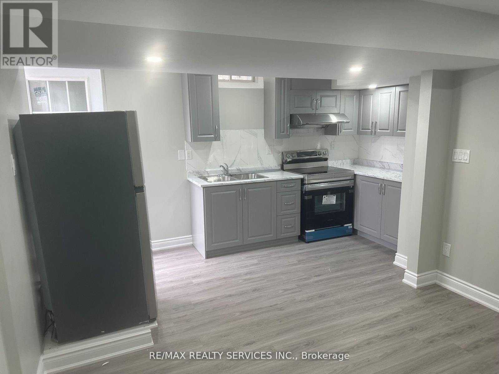 A kitchen with a black refrigerator and wooden flooring.