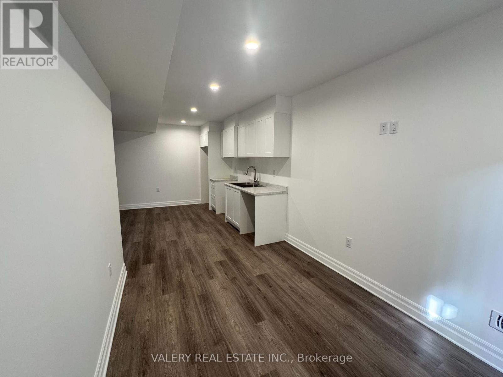 A room with wooden flooring and white walls, with a kitchenette in the corner.