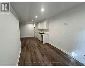 A room with wooden flooring and white walls, with a kitchenette in the corner.