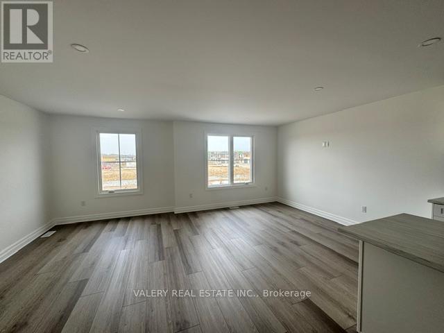 A spacious room with wood flooring and two windows.