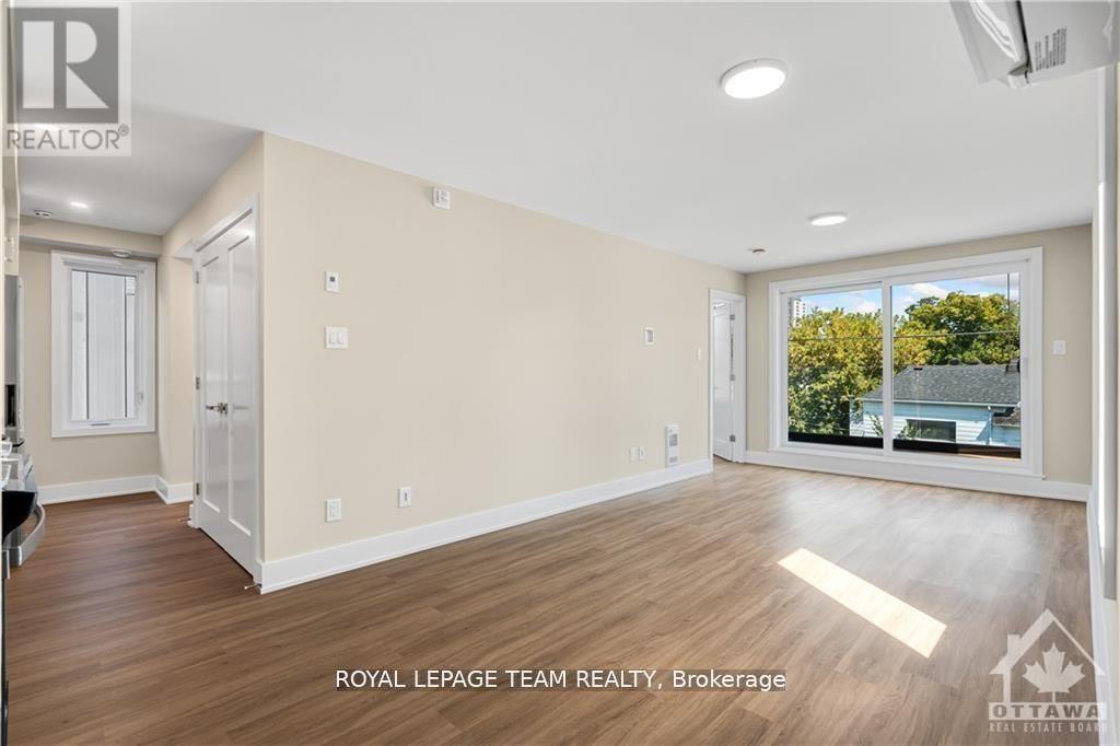 A spacious room with wooden flooring and a large window overlooking a backyard.
