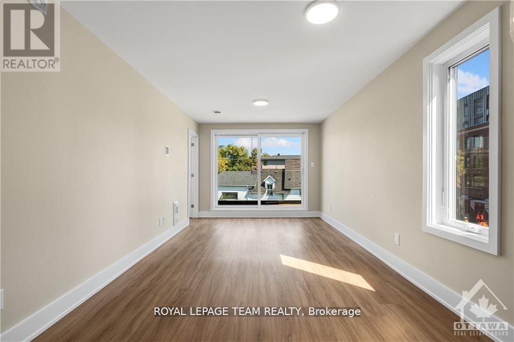 A spacious room with wooden flooring and a large window overlooking a balcony.