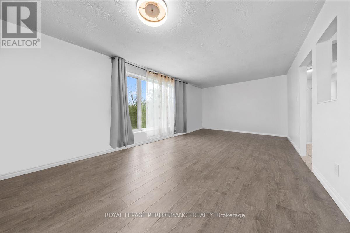 A spacious room with wooden flooring and a window with curtains.