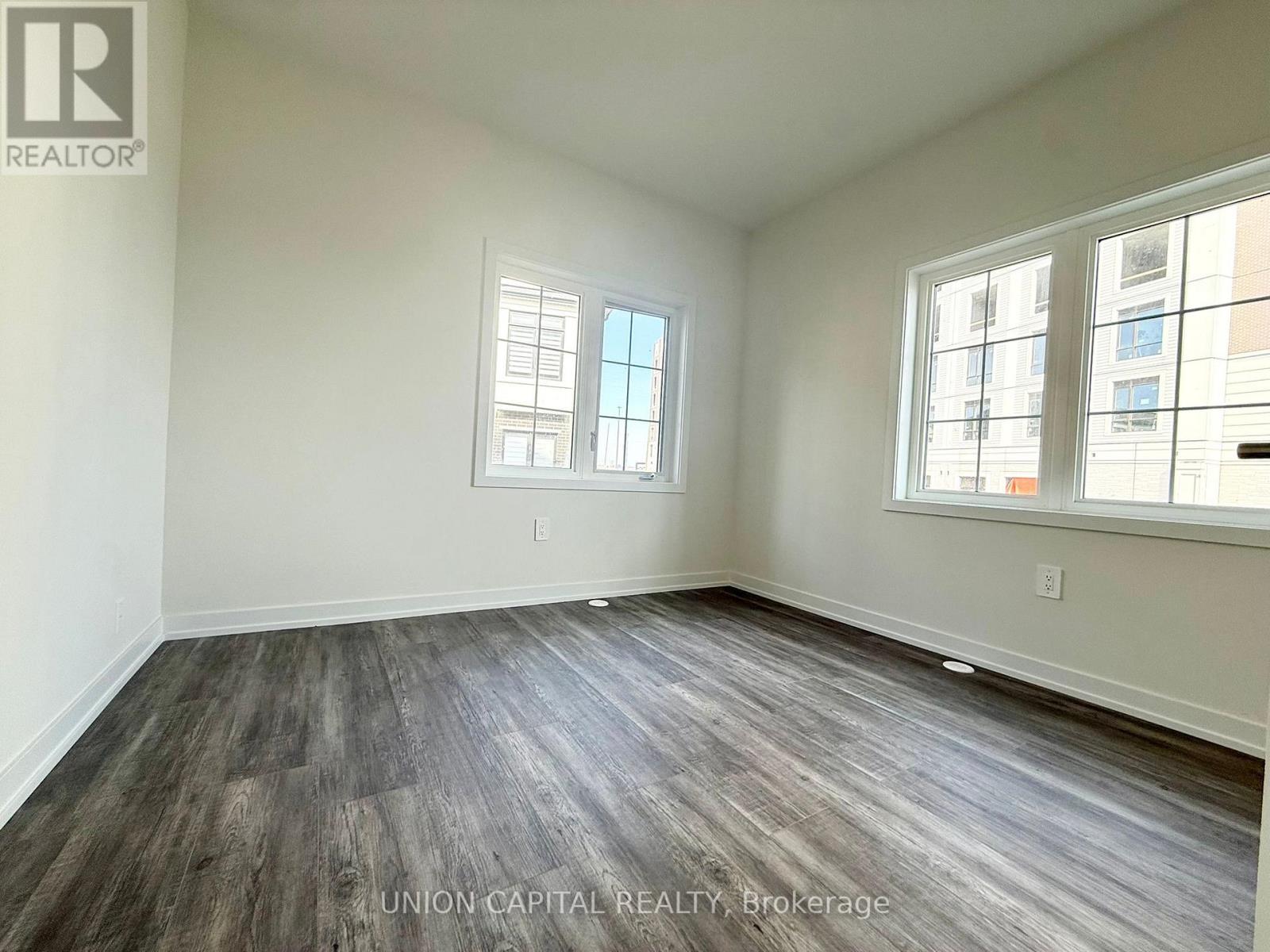 A room with wooden flooring and two windows.