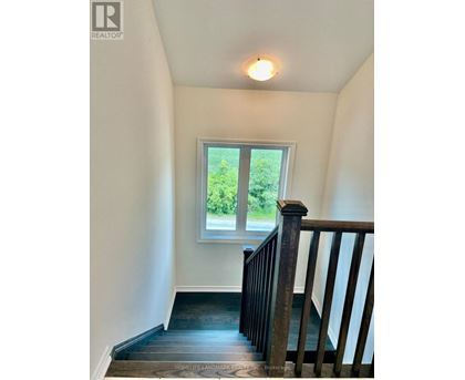 A staircase with a wooden railing leads to a window with a view of greenery outside.
