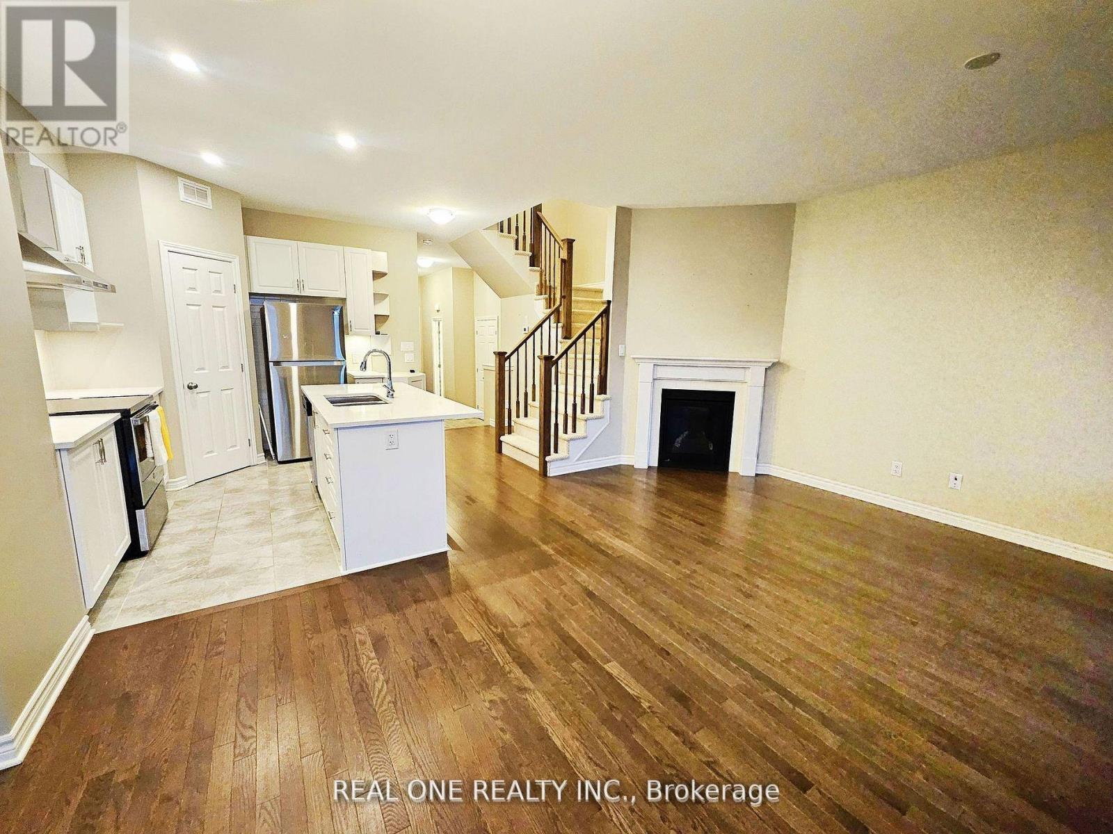 A spacious living room with wood flooring and a staircase in the background.