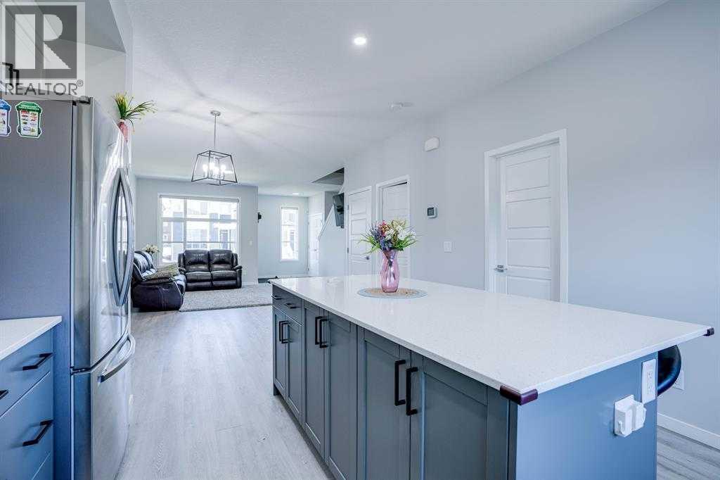 A kitchen with a refrigerator on the left and a counter with a vase of flowers on it.