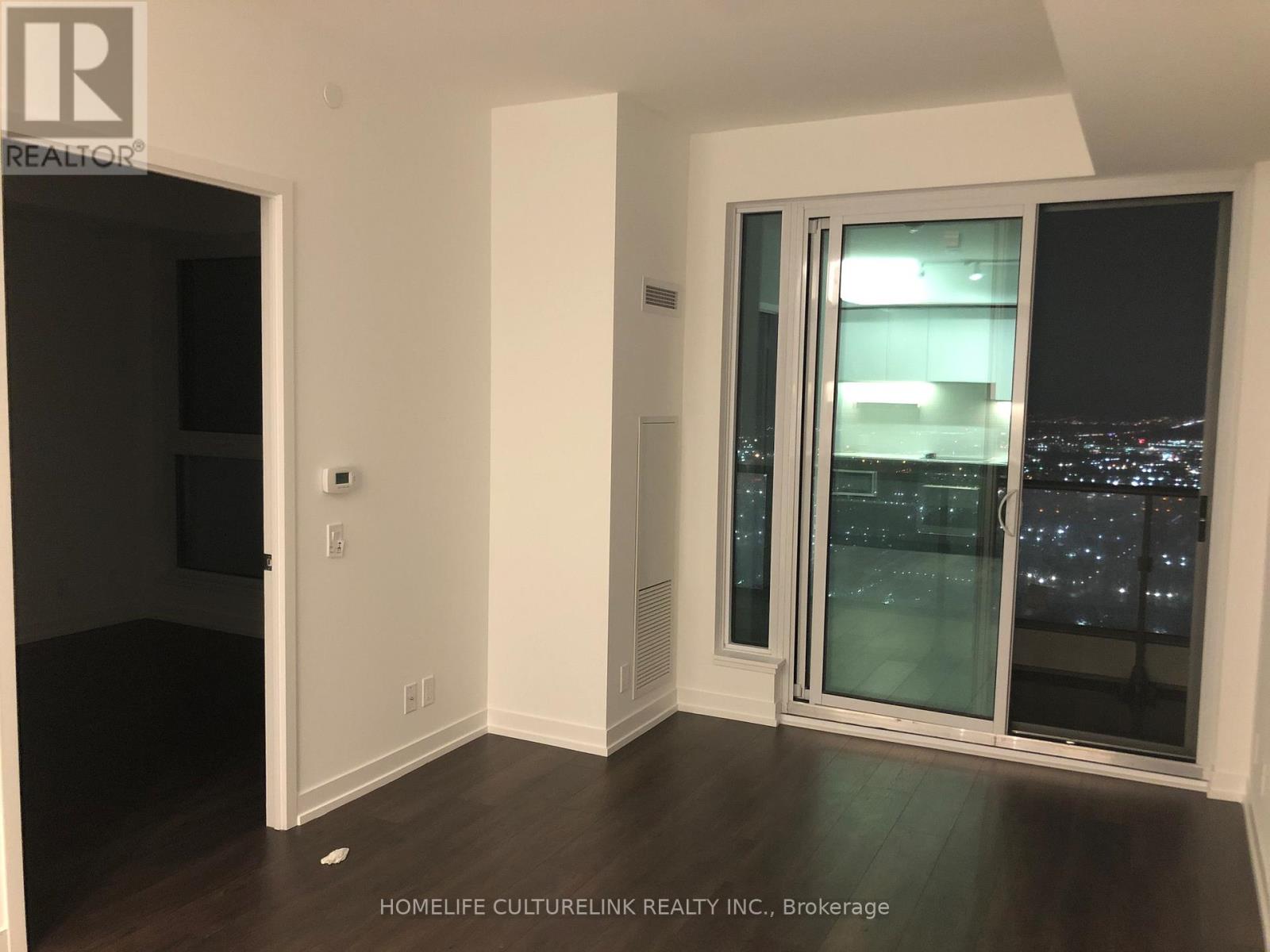 A room with a sliding glass door leading to a cityscape at night.