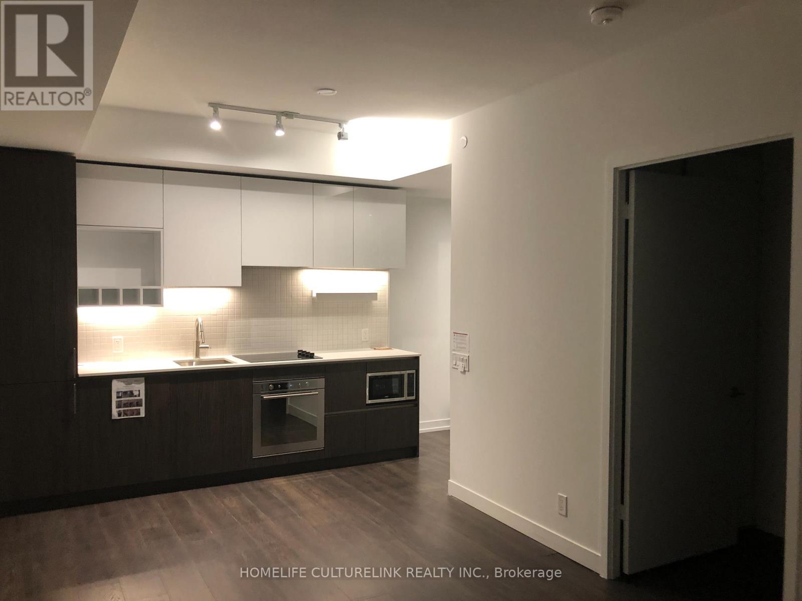 A modern kitchen with dark wood floors and white walls.