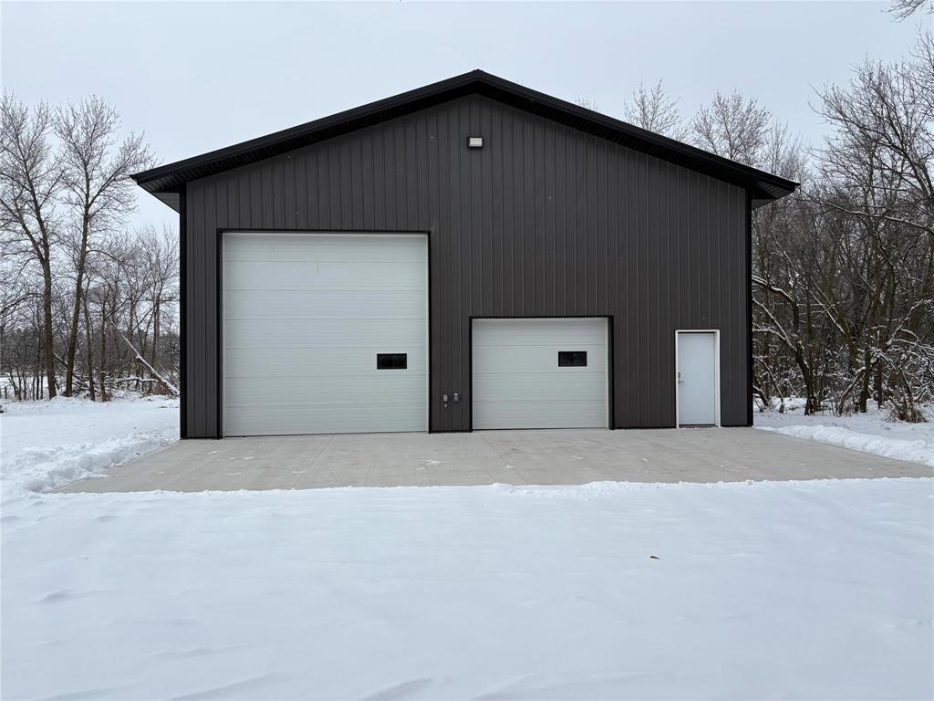A black building with two white garage doors in the snow.