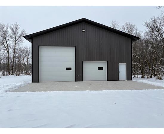 A black building with two white garage doors in the snow.