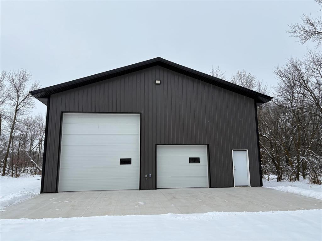 A black building with two white garage doors in the snow.