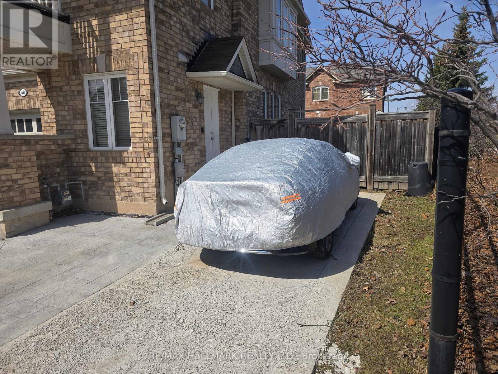A car covered in a tarp is parked in front of a house with a RE/MAX sign.