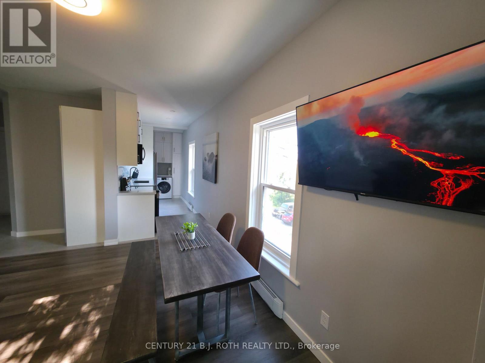 A dining room with a wooden table and chairs, a flat screen TV displaying an image of lava, and a window letting in natural light.