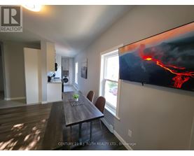 A dining room with a wooden table and chairs, a flat screen TV displaying an image of lava, and a window letting in natural light.