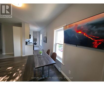 A dining room with a wooden table and chairs, a flat screen TV displaying an image of lava, and a window letting in natural light.