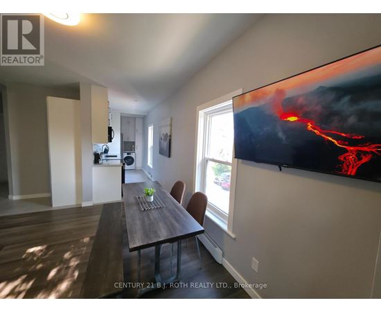 A dining room with a wooden table and chairs, a flat screen TV displaying an image of lava, and a window letting in natural light.