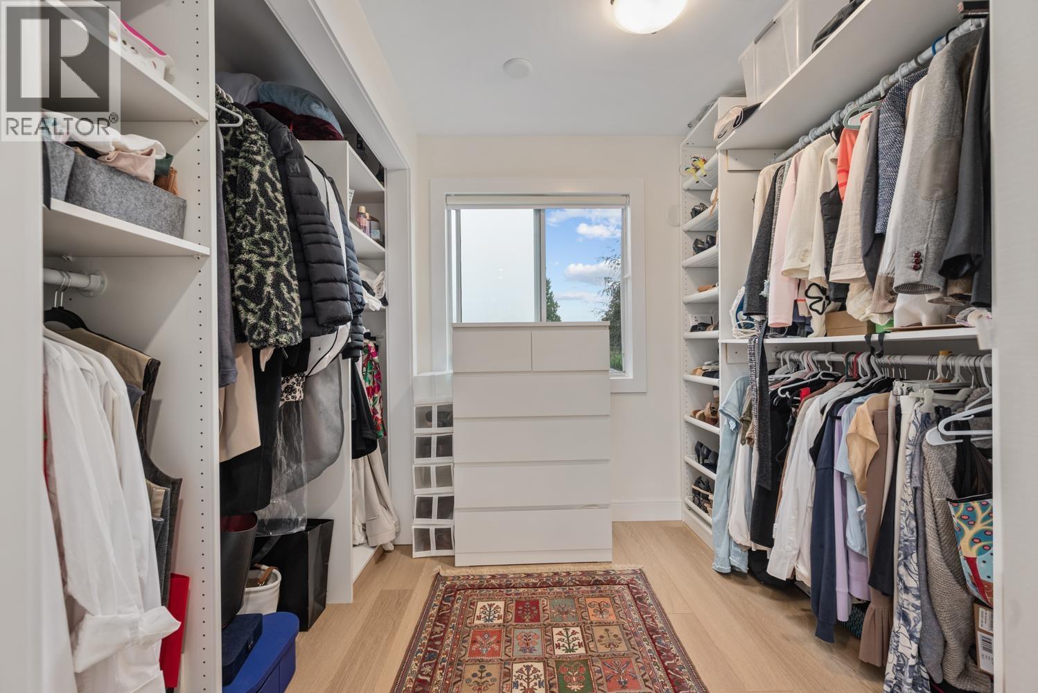 A spacious walk-in closet with a rug on the floor and clothes hanging on shelves.