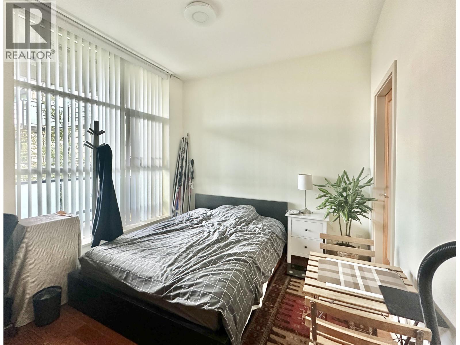 A bedroom with a bed, chair, and window with blinds.