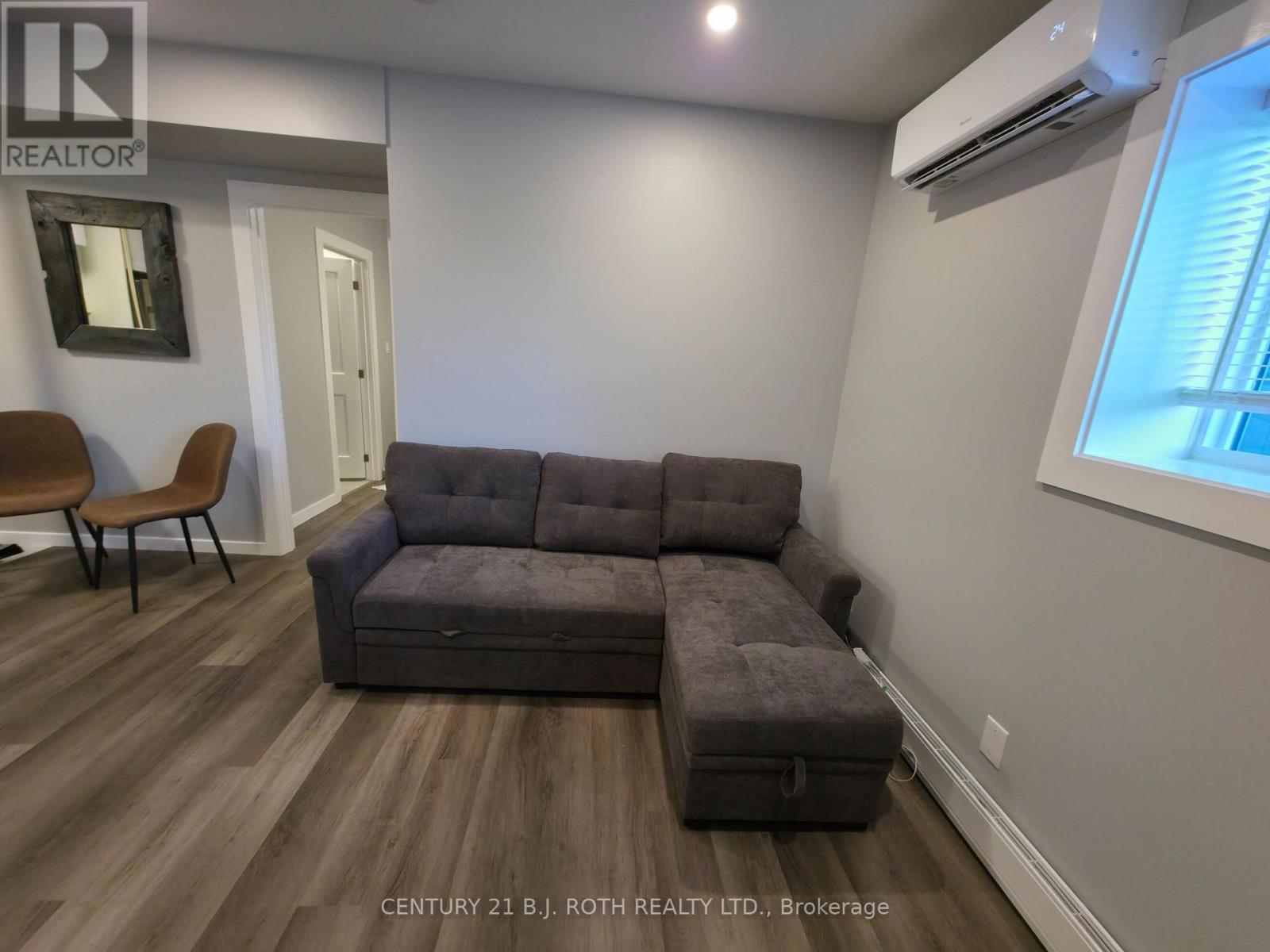A grey couch in a room with wooden flooring and a window.