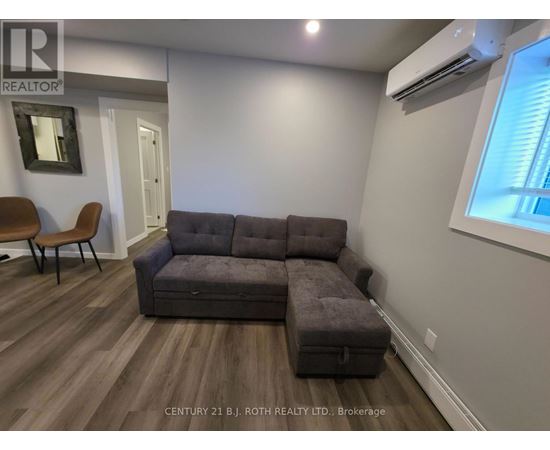 A grey couch in a room with wooden flooring and a window.