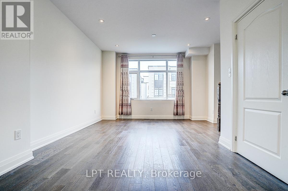 A spacious room with wooden flooring and a large window with curtains.