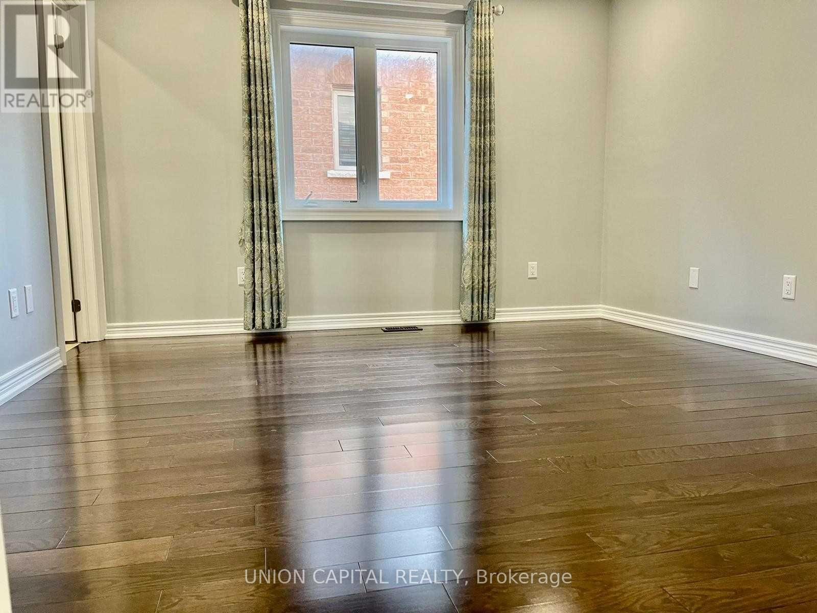 A room with wooden flooring and a window with a view of a brick building outside.