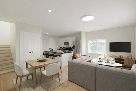 A modern living room with a grey couch, a wooden dining table with chairs, and a kitchen area in the background.