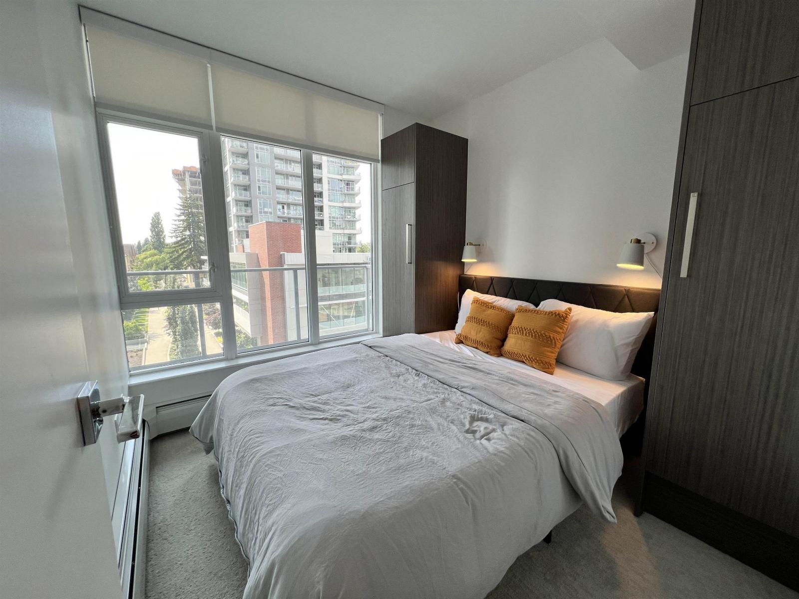A bedroom with a large bed and a view of a building outside the window.