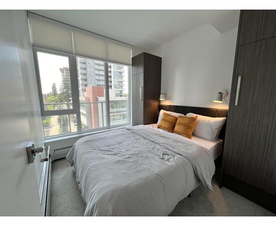 A bedroom with a large bed and a view of a building outside the window.