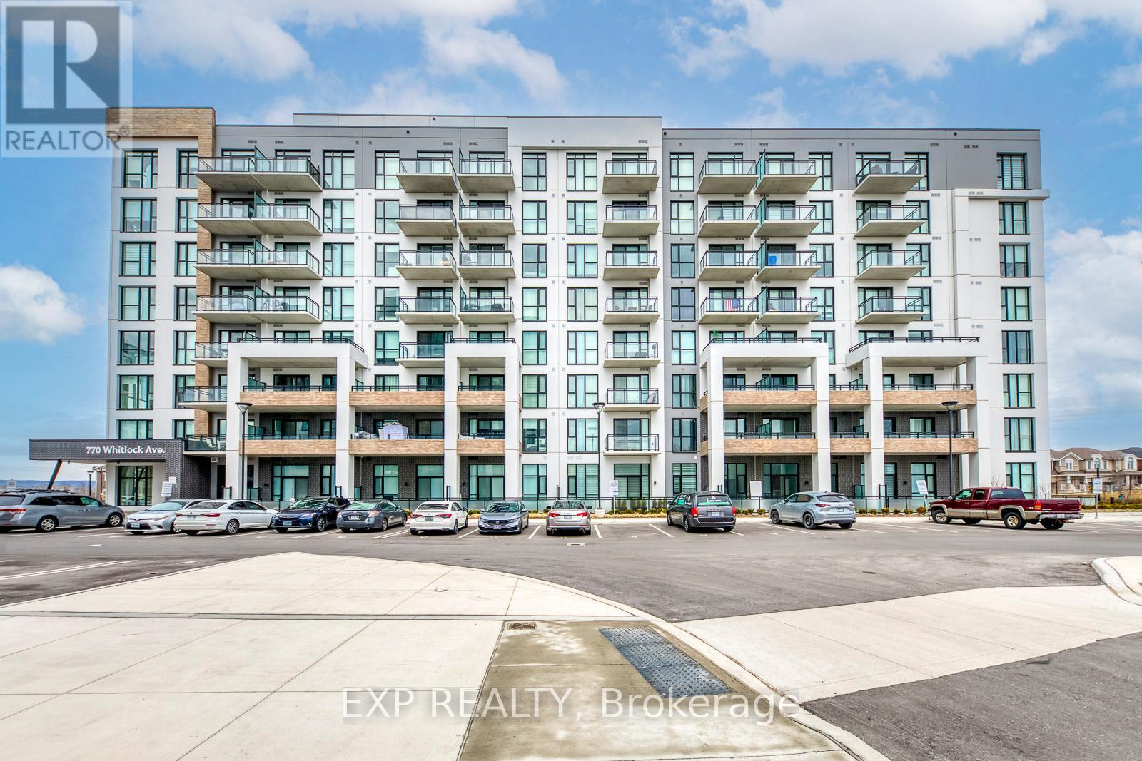 A large, modern apartment building with multiple balconies and a parking lot in front.