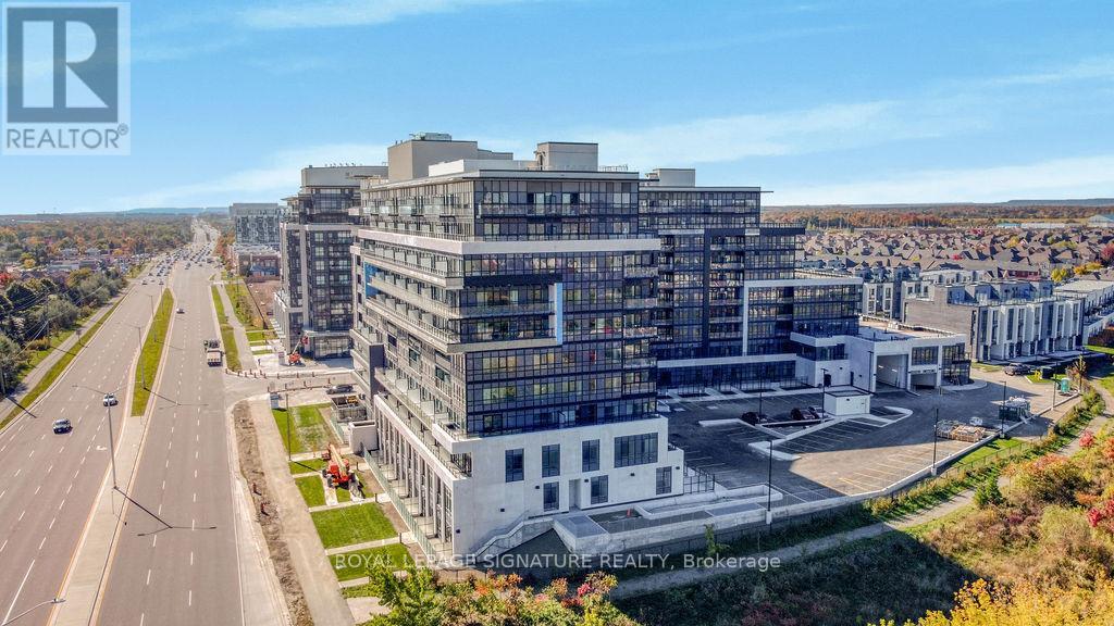 A large, modern building with glass windows is situated on a road with a clear sky above.