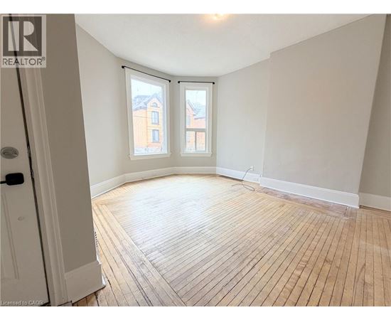 A room with wooden flooring and a window overlooking a building.