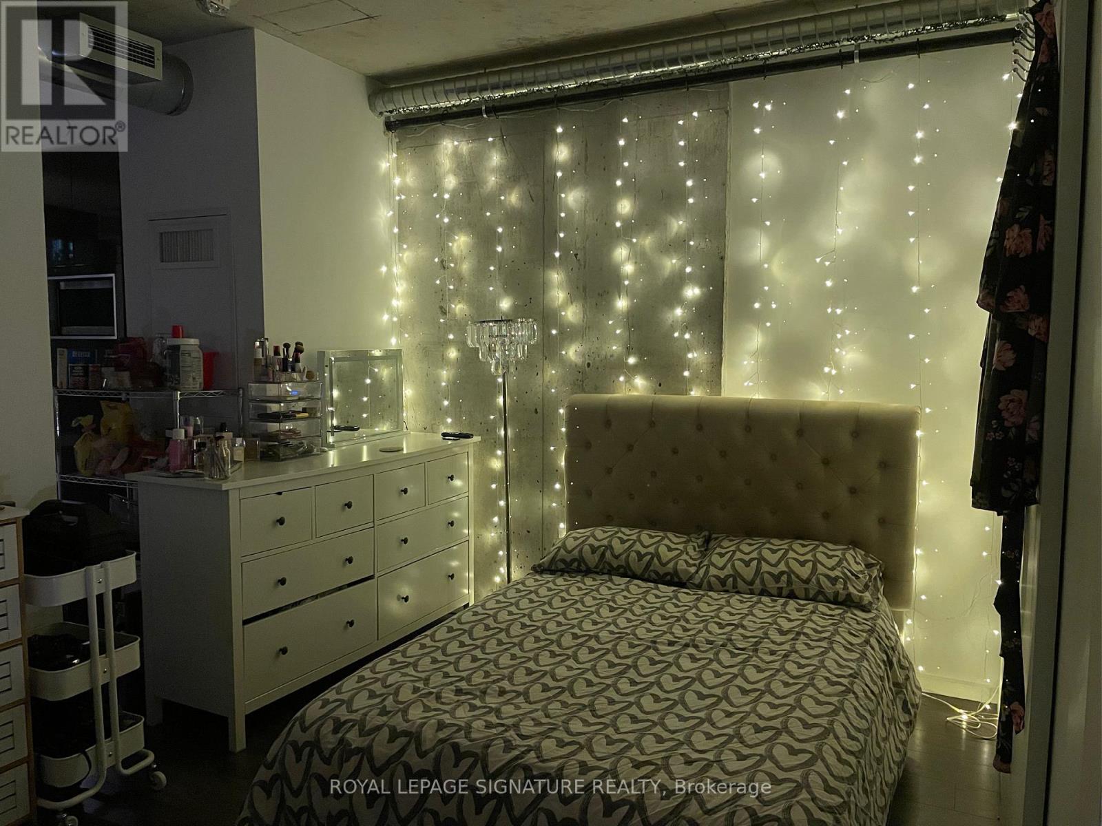 A bedroom with a bed, dresser, and a window with lights.