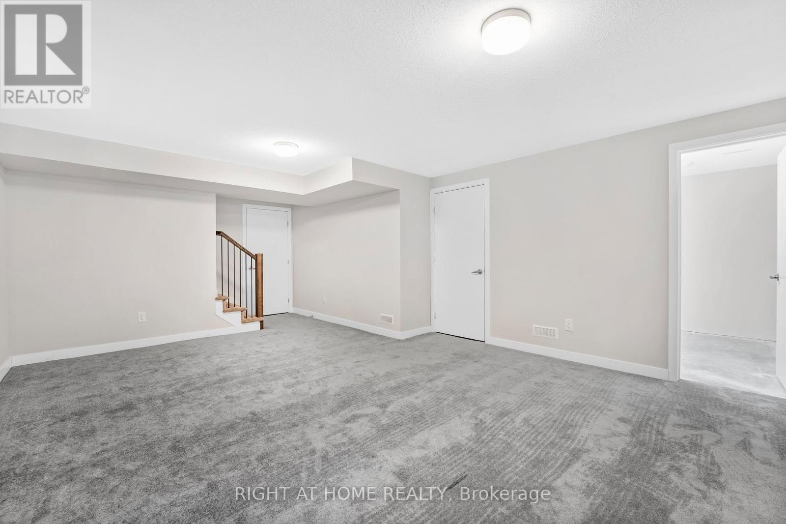 A spacious room with a carpeted floor and a staircase with a metal railing.