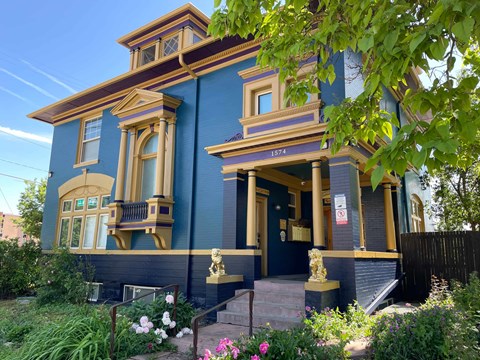 A blue Victorian style house with a front porch and a small garden.
