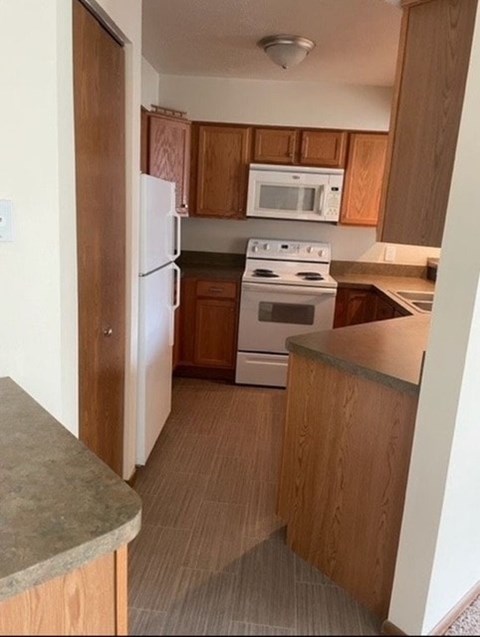 A kitchen with a white refrigerator, white microwave, white stove and wooden cabinets.