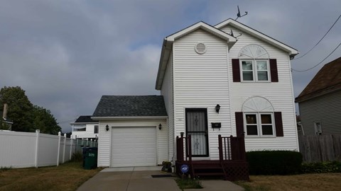 A white house with a black roof and a brown fence.