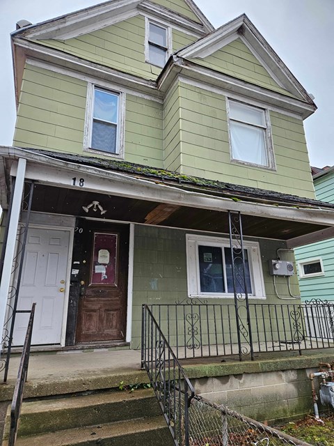 A green two-story house with a white door and window.