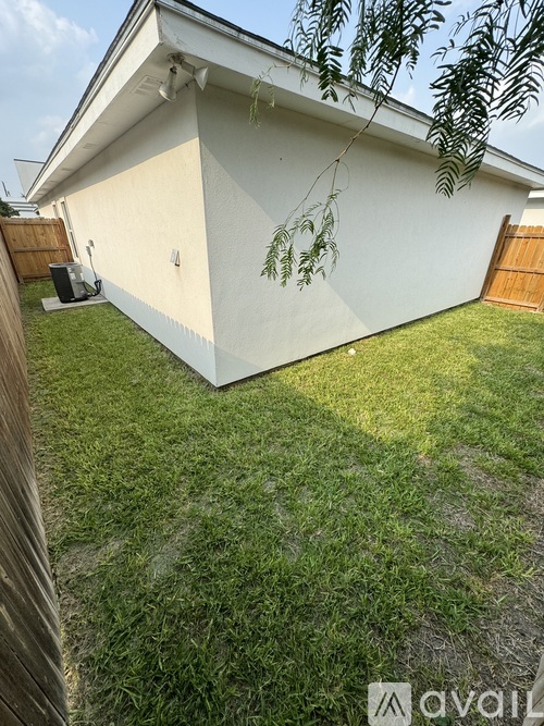 A backyard with a white house, green grass, and a wooden fence.