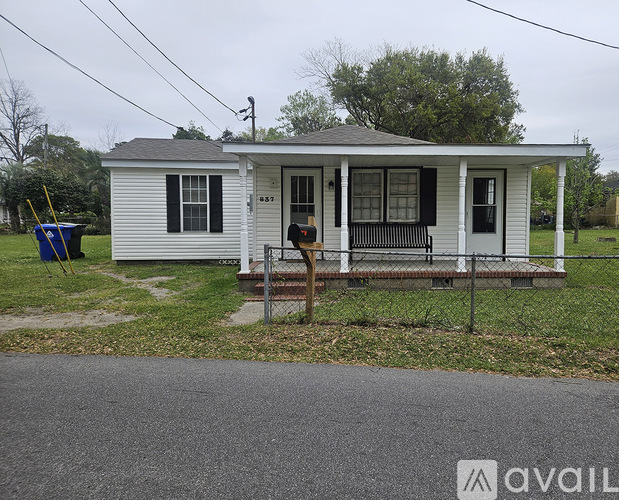 A small white house with a porch and a fence in front.