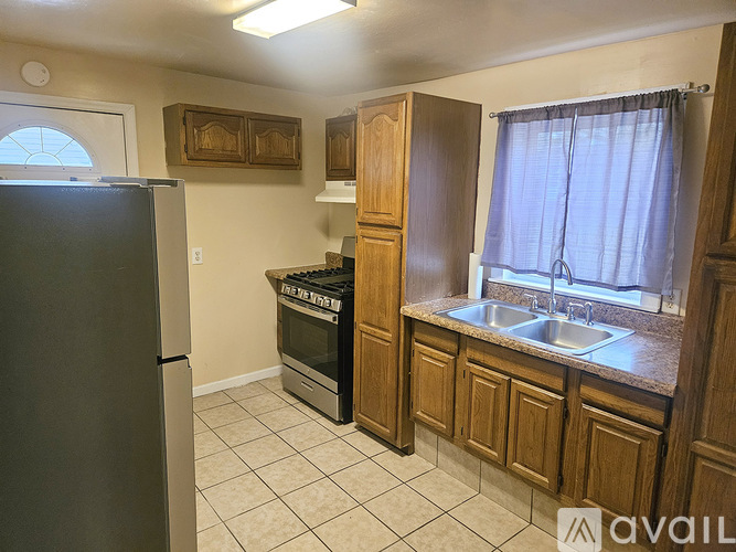 A kitchen with a black refrigerator, wooden cabinets, and a window with curtains.